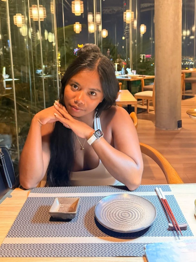 Vivian Dolor at a cafe table, chin on hand, smiling at the camera.